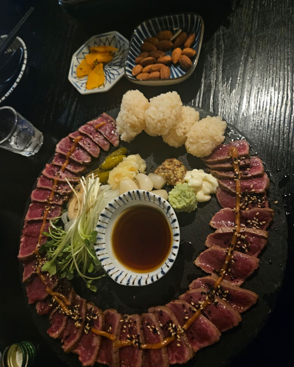 대구광역시 달성군 이자카야 대담히 다사점 대구 혼술 메뉴인 소고기 타타키. 어두운 조명 아래 나무 테이블 위 검은 돌판에 차려진 선분홍빛 고기와 와사비, 1인 다찌석 식사 구성.