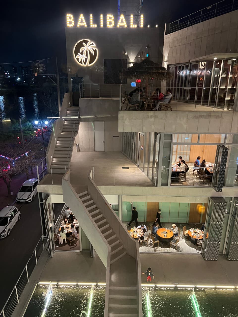 대구광역시 동구 발리발리 동촌유원지점 대구 야경 조명 아래 테라스와 창가 1인석. 분수와 야자수 간판이 있는 기타 업종 매장 다찌석에서 혼술 하는 상황.