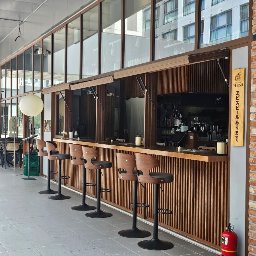 인천광역시 연수구 siori 인천 요리주점 외부 다찌석. 따뜻한 조명 아래 나무 질감의 긴 카운터와 의자가 나열된 1인 혼술 공간.