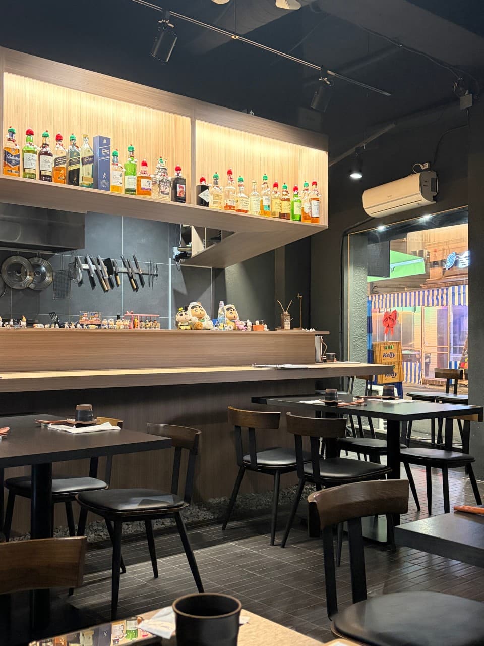 인천광역시 남동구 우자카야 인천 이자카야의 전구색 조명 아래 마련된 1인 다찌석과 테이블. 벽면의 위스키 병들과 캐릭터 소품이 놓인 카운터에서 즐기는 혼술 상황.