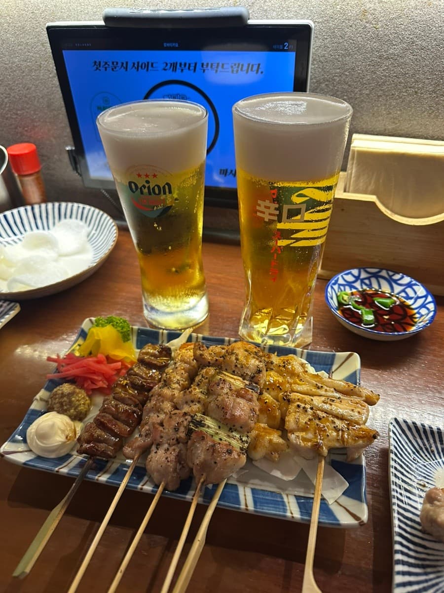 인천광역시 연수구 로바타키요 송도본점 인천 이자카야 다찌석에 놓인 1인 꼬치구이와 생맥주. 상단 조명 아래 윤기 흐르는 야키토리와 조밀한 맥주 거품이 차려진 혼술 상황.