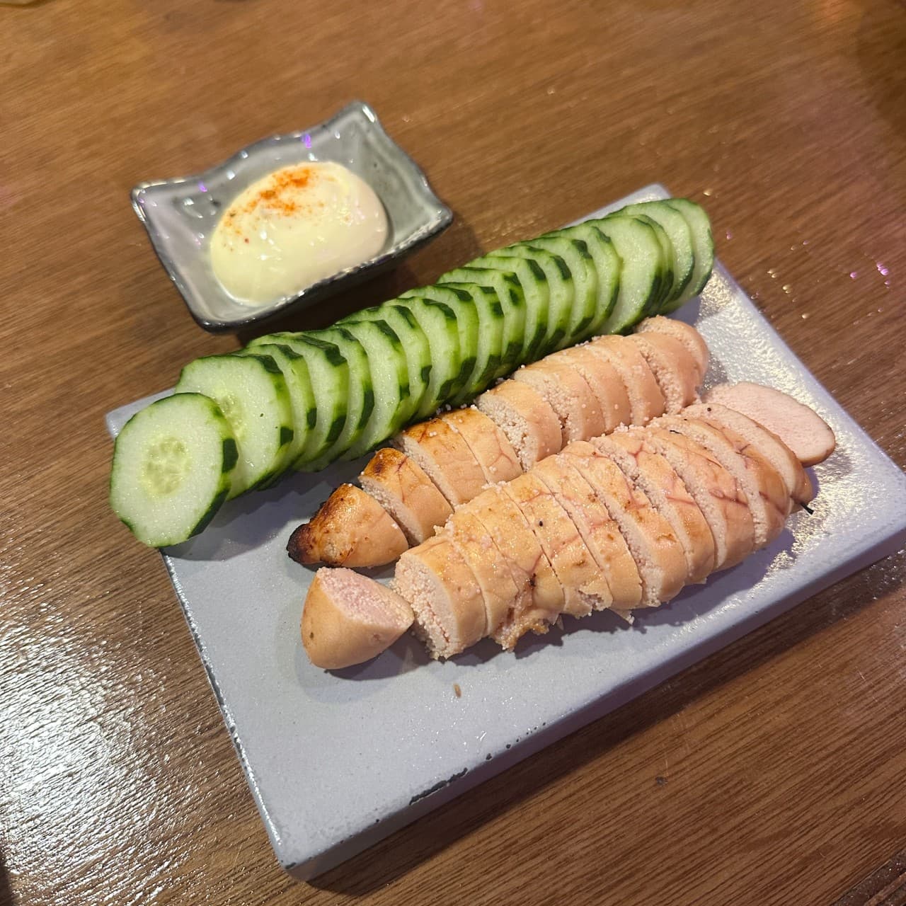 인천광역시 영종구 이자카야 시마네코 인천. 따뜻한 조명 아래 나무 다찌석에서 혼술로 즐기는 노릇하게 구운 명란구이와 얇게 썬 오이, 마요네즈 소스.