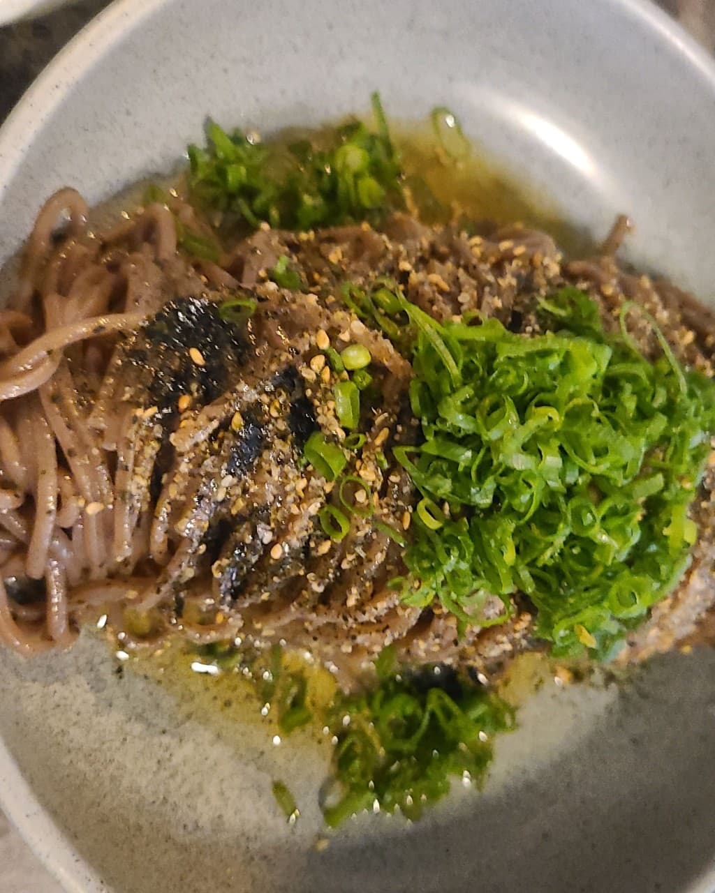 인천광역시 부평구 요리주점 스몰톡소셜클럽 인천의 다찌석 조명 아래 놓인 들기름 막국수. 잘게 썬 쪽파와 김가루가 뿌려진 메밀면을 1인 혼술로 즐기는 상황.