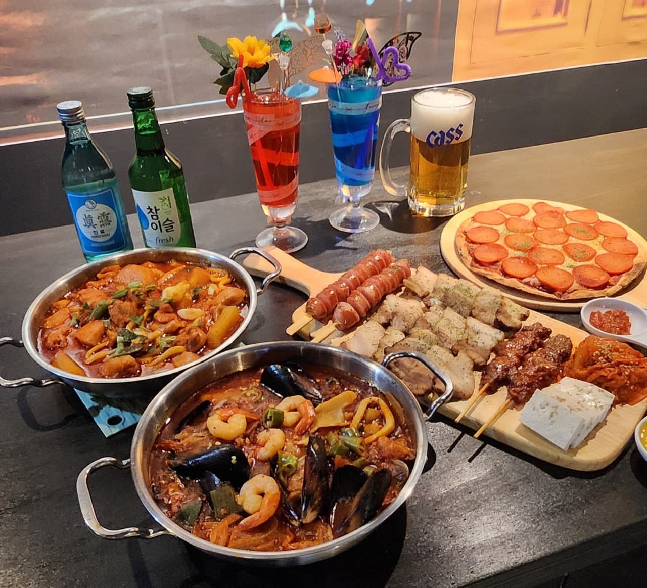 인천광역시 부평구 요리주점 스카이루프탑 부평점 인천의 1인 다찌석. 해물찜, 닭볶음탕, 페퍼로니 피자와 꼬치구이 등 정갈한 안주와 소주, 칵테일이 차려진 테이블에서 혼술을 즐기는 상황.