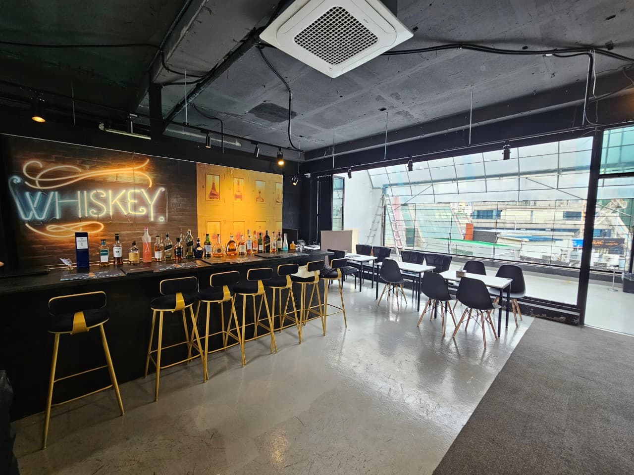 인천광역시 부평구 요리주점 스카이루프탑 부평점 인천의 Whiskey 네온사인 아래 바 테이블과 위스키병들. 1인 혼술용 높은 의자와 창밖 전경이 보이는 실내 전경