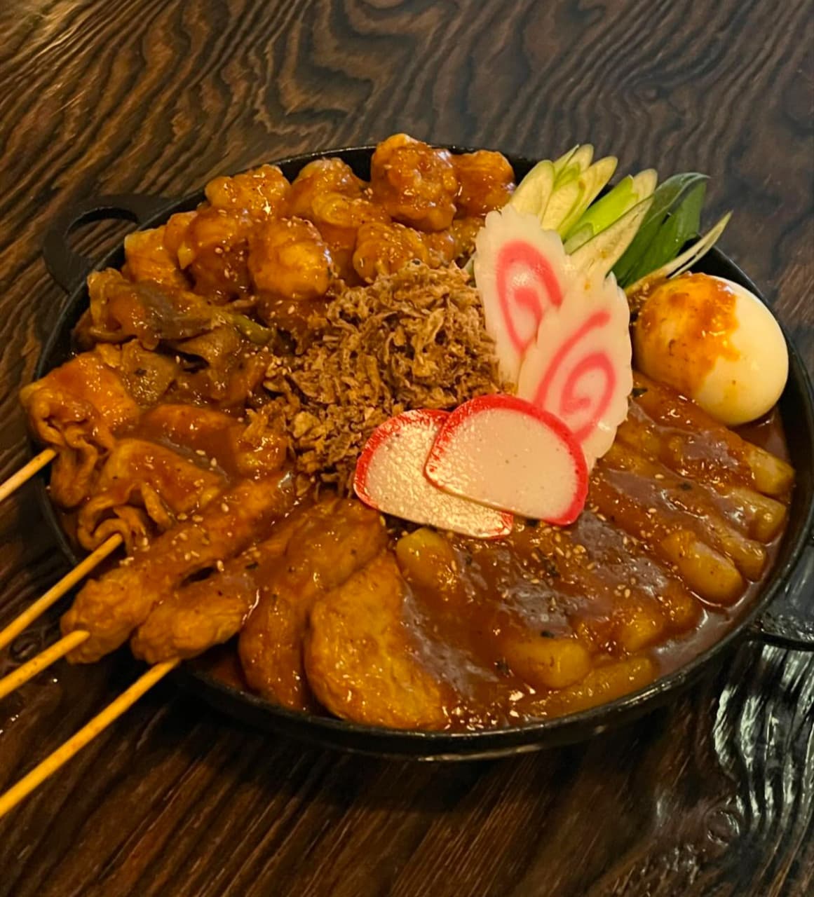 인천광역시 서해구 이고식당 인천 이자카야 다찌석 조명 아래 놓인 1인 혼술 메뉴. 어묵 꼬치와 떡, 나루토마끼와 삶은 달걀이 담긴 철판 전골의 질감과 나무 테이블 무늬가 강조된 상황.