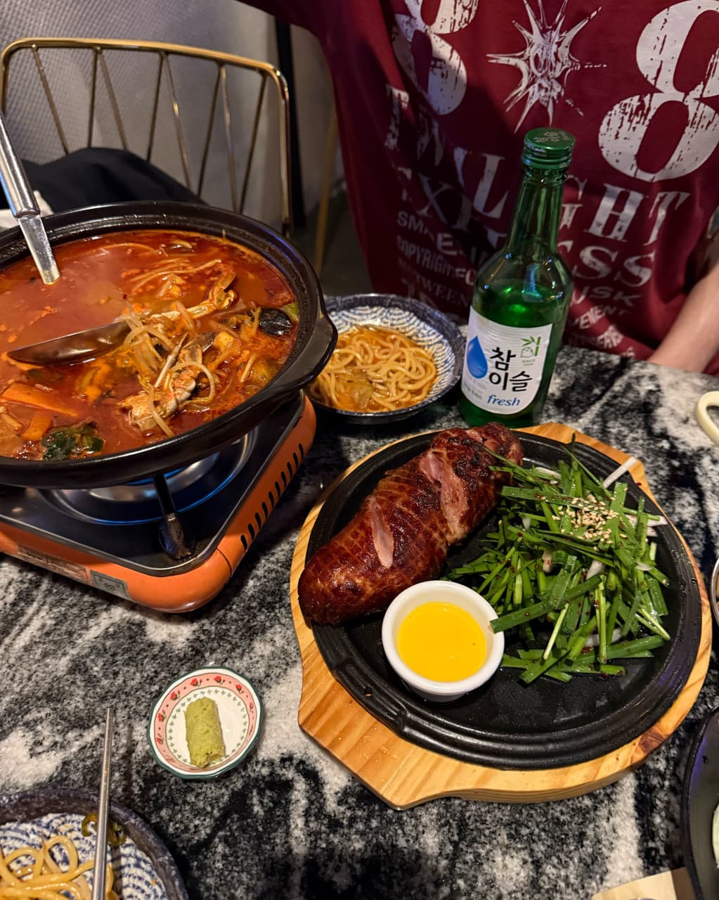 인천광역시 영종구 요리주점 촤랑 인천 1인석에서 즐기는 혼술. 버너 위 빨간 국물 요리와 부추를 곁들인 고기 구이, 소주 한 병이 대리석 테이블에 차려진 상황.