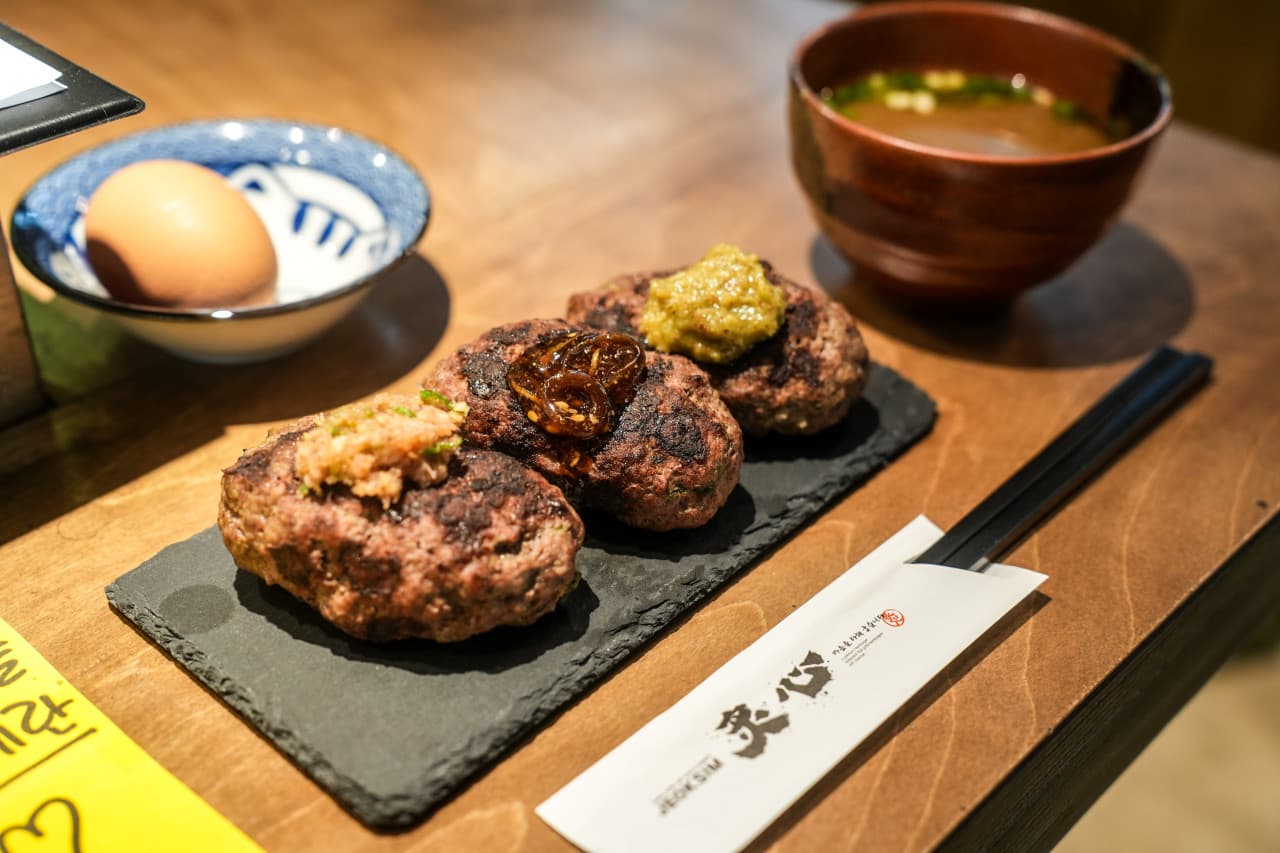 제주특별자치도 서귀포시 이자카야 적심 제주 1인 다찌석. 나무 테이블 위 조명을 받아 윤기가 흐르는 세 가지 토핑의 함박 스테이크와 날달걀, 장국이 차려진 혼술 현장.