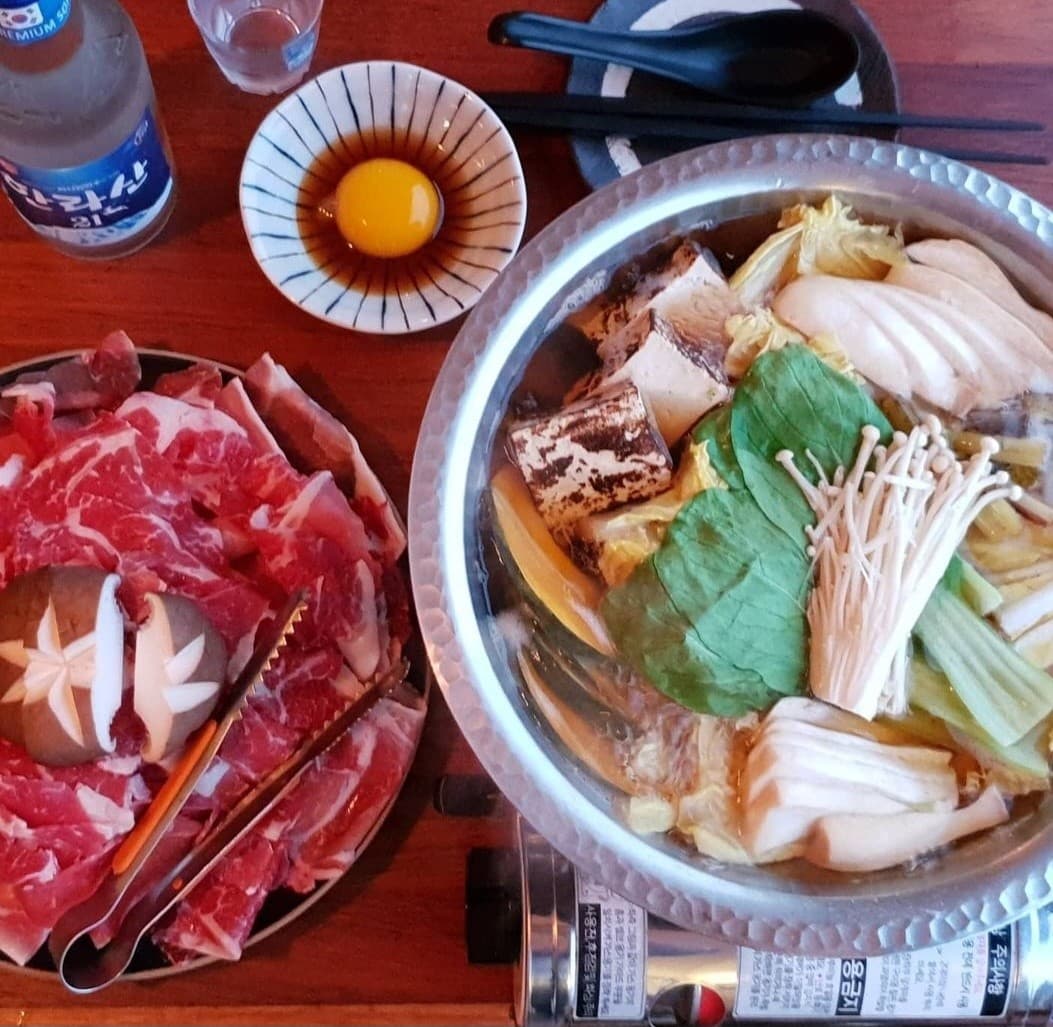 제주특별자치도 제주시 우미노식탁 제주 이자카야 다찌석에 차려진 1인 스키야키와 한라산 소주. 선홍빛 소고기, 신선한 채소, 노른자 소스가 담긴 목재 테이블 위 혼술 상차림.