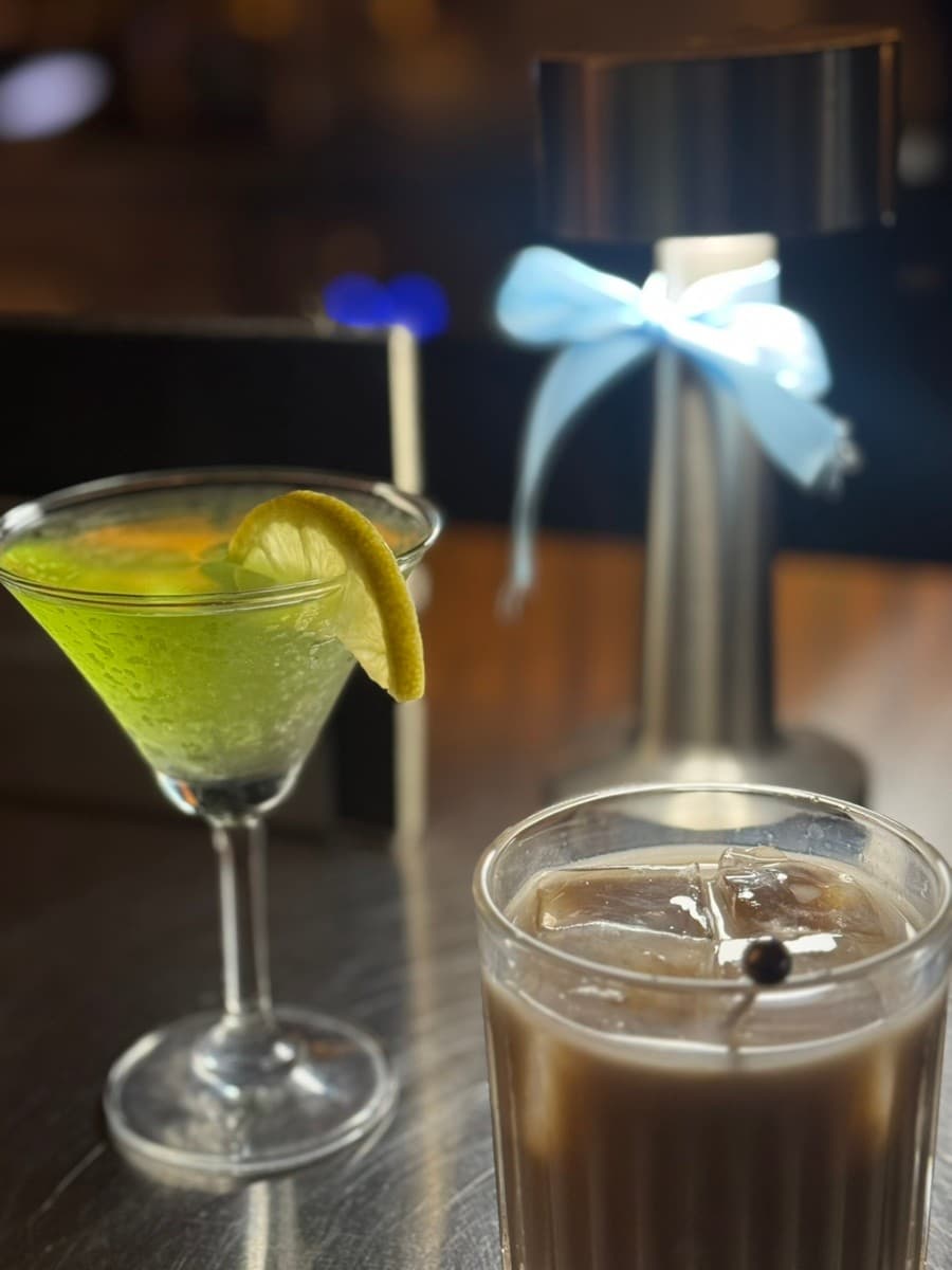 제주특별자치도 제주시 공과사 제주혼술바 바(Bar) 다찌석 조명 아래 레몬을 곁들인 초록색 칵테일과 얼음이 담긴 1인 술잔이 놓여 있음