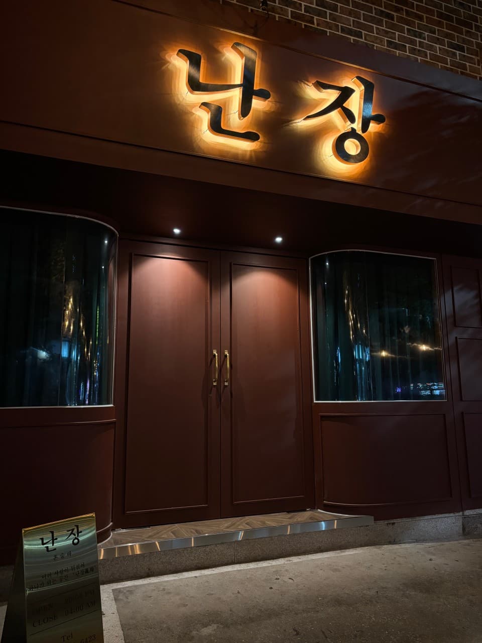 강원특별자치도 강릉시 난장혼술바 강릉점 바(Bar) - 어두운 밤 금색 조명이 빛나는 간판과 짙은 갈색 문, 곡선 유리창이 배치된 혼술 전문점 입구