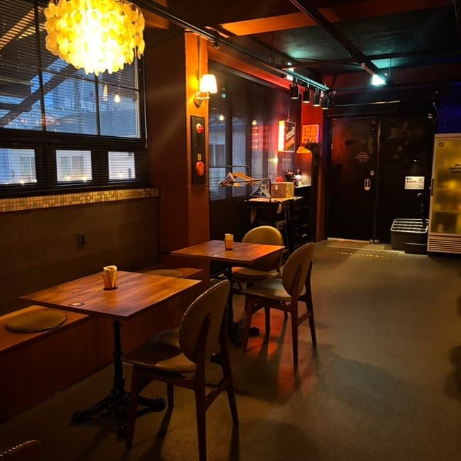 강원특별자치도 속초시 바(Bar) 주경야독 내부. 노란 원형 조명이 내려오는 창가 벤치와 1인 테이블. 어두운 실내 속 목재 가구로 구성된 혼술 공간.