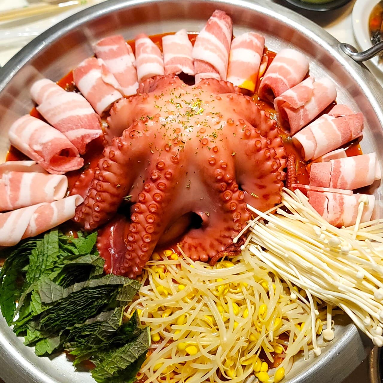 강원특별자치도 동해시 어달 옆 포차 - 조명 아래 1인 다찌석에 차려진 통문어와 대패삼겹살. 콩나물, 깻잎, 팽이버섯이 담긴 철판 요리를 즐기는 혼술 포장마차 상황.