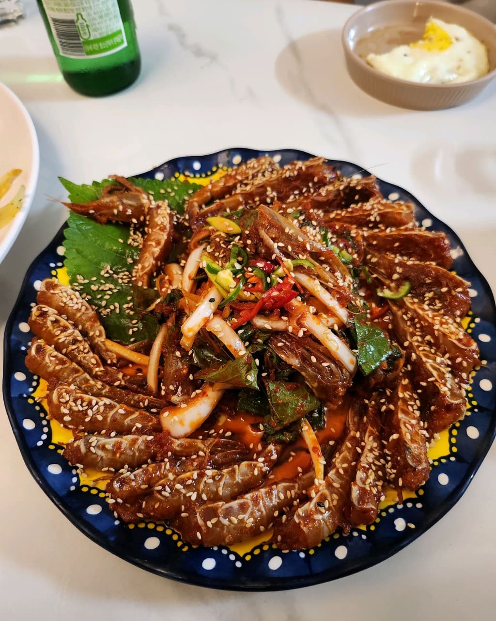 강원특별자치도 동해시 이자카야 이야기고래의 1인 혼술. 참깨가 뿌려진 붉은 새우장과 소주병이 놓인 흰색 테이블 다찌석에 음식이 차려진 상황.