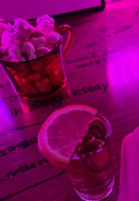 강원특별자치도 강릉시 혼술 바(Bar) 강릉현대정수기 - 보라색 조명 아래 낙서된 다찌석과 레몬을 얹은 술잔, 팝콘이 놓인 1인석 풍경