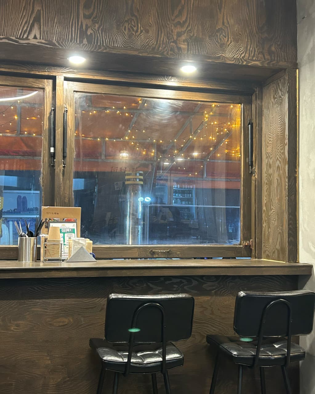 강원특별자치도 강릉시 맥주 호프 춘몽의 나무 다찌석과 1인용 의자. 상단 조명 아래 창밖 전구가 보이는 창가 좌석에서 혼술을 즐기는 상황.