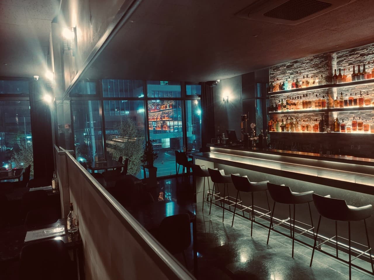 강원특별자치도 춘천시 Whisky no.213 바(Bar)의 하단 조명이 비추는 긴 다찌석과 벽면 위스키 진열장. 통창 밖 야경을 배경으로 구성된 1인석에서 혼술을 즐기는 상황.