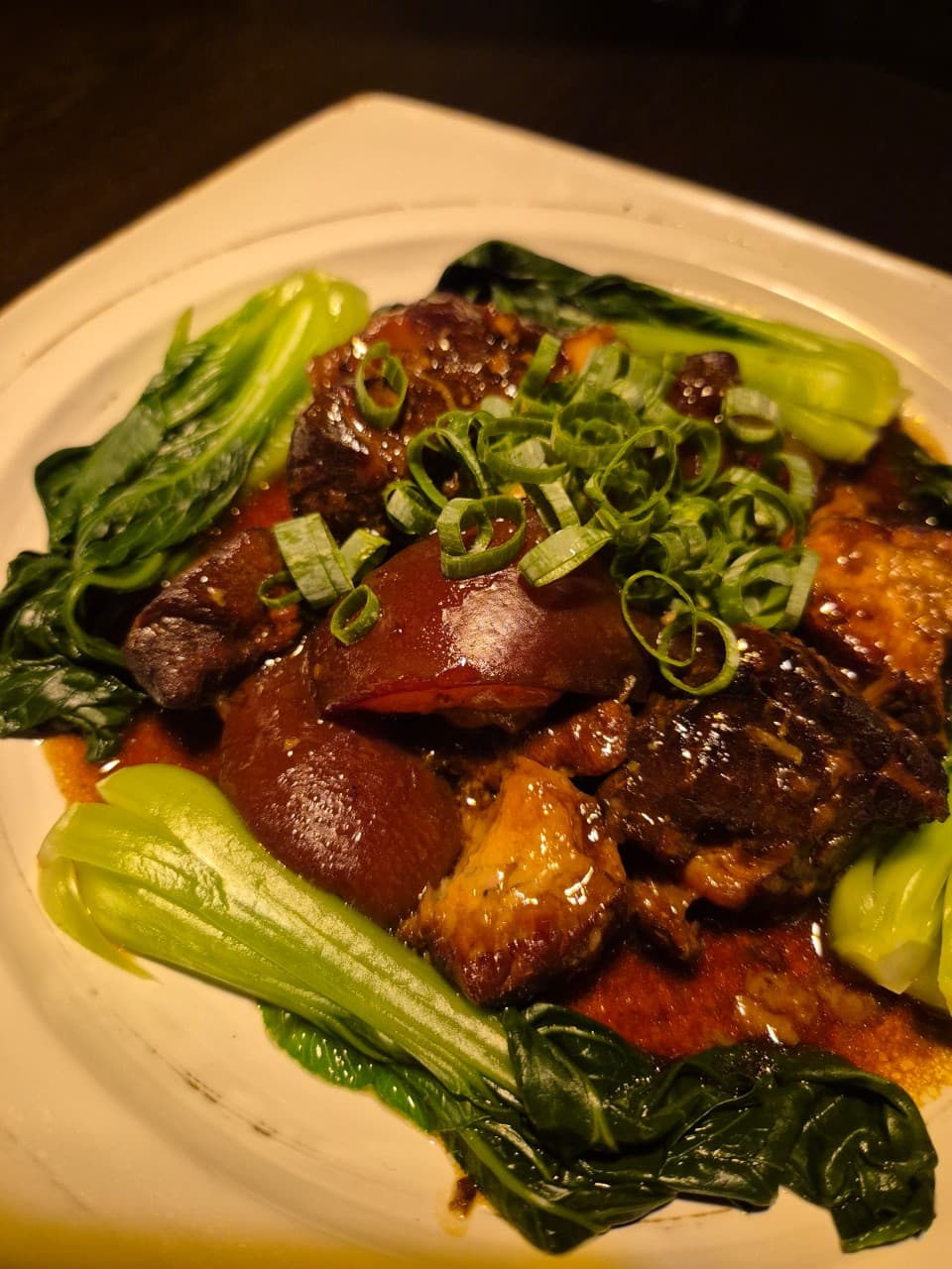 강원특별자치도 강릉시 잉걸불 1인 다찌석 혼술. 노란 조명 아래 진한 소스의 고기 찜과 청경채, 파 고명이 담긴 기타 요리의 질감이 돋보이는 구성.