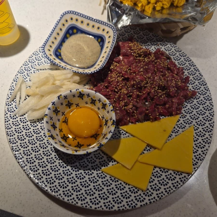 강원특별자치도 영월군 니코니코 이자카야 혼술 - 조명 아래 다찌석 테이블 위 문양 접시에 담긴 육회와 노른자, 치즈, 배가 어우러진 1인 메뉴