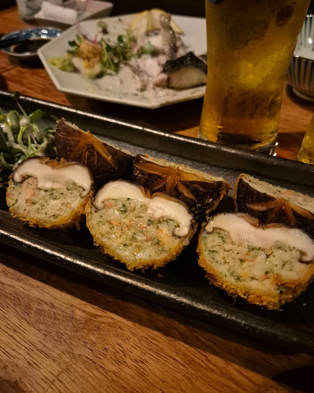강원특별자치도 속초시 월간속초 요리주점 다찌석 조명 아래 놓인 표고버섯 튀김과 생맥주. 1인 혼술 상황의 나무 테이블 위 정갈하게 차려진 안주와 술의 질감을 표현함.