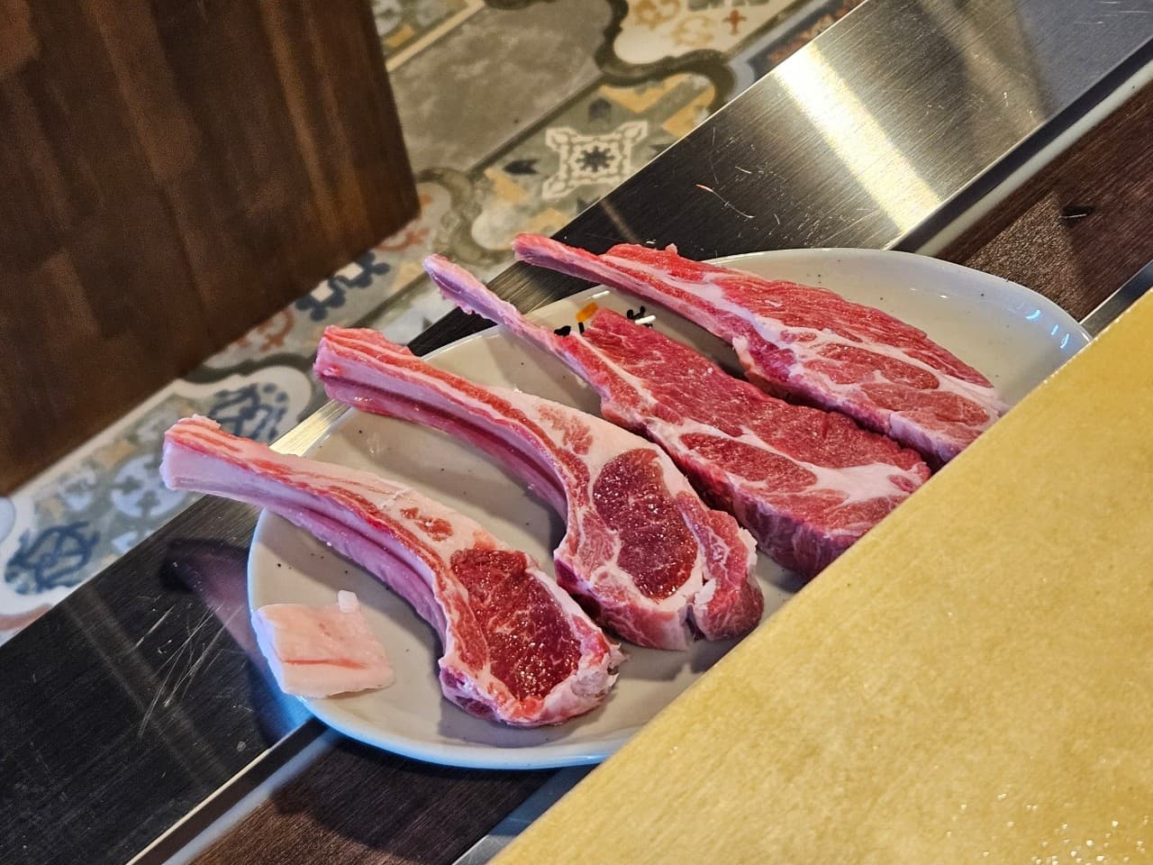 경상남도 창원시 징스램 상남점 1인 다찌석 조명 아래 차려진 선홍빛 양갈비. 고기의 육질과 기타 구성을 강조하여 혼술 중인 상황을 보여줌.