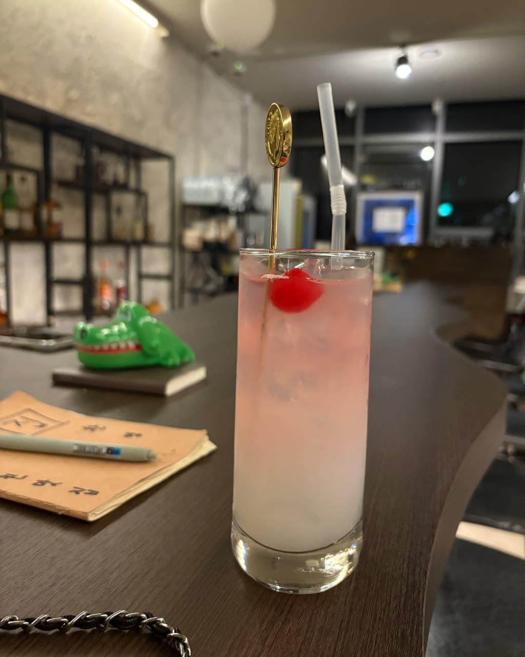 경상남도 창원시 꼼바혼술바 창원상남점 바(Bar) 다찌석 위 체리가 담긴 핑크빛 칵테일. 실내 조명 아래 1인 좌석에서 혼술을 즐기는 상황을 묘사함.