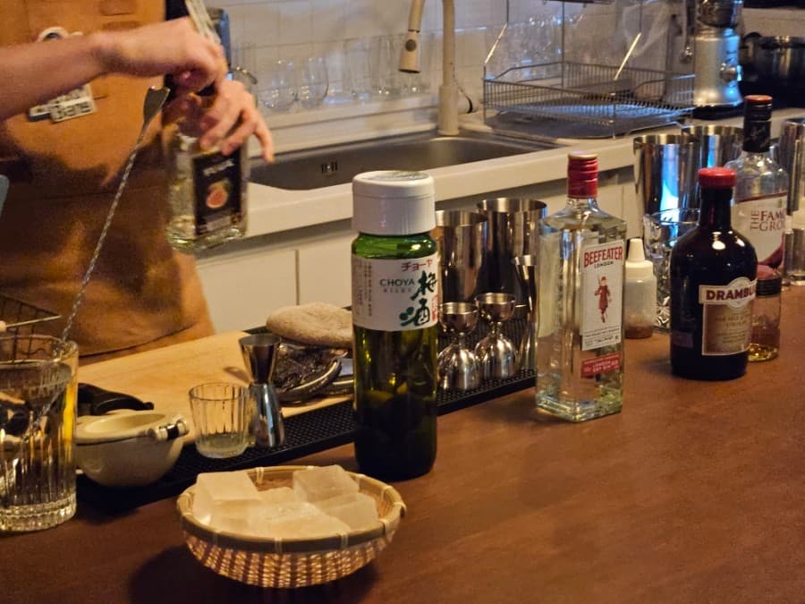 경상남도 진주시 혼술 바(Bar) 우심방의 나무 다찌석 위 비피터 진과 초야 매실주. 바구니에 담긴 투명한 각얼음과 칵테일 기구 옆에서 바텐더가 음료를 제조하는 1인석 현장.