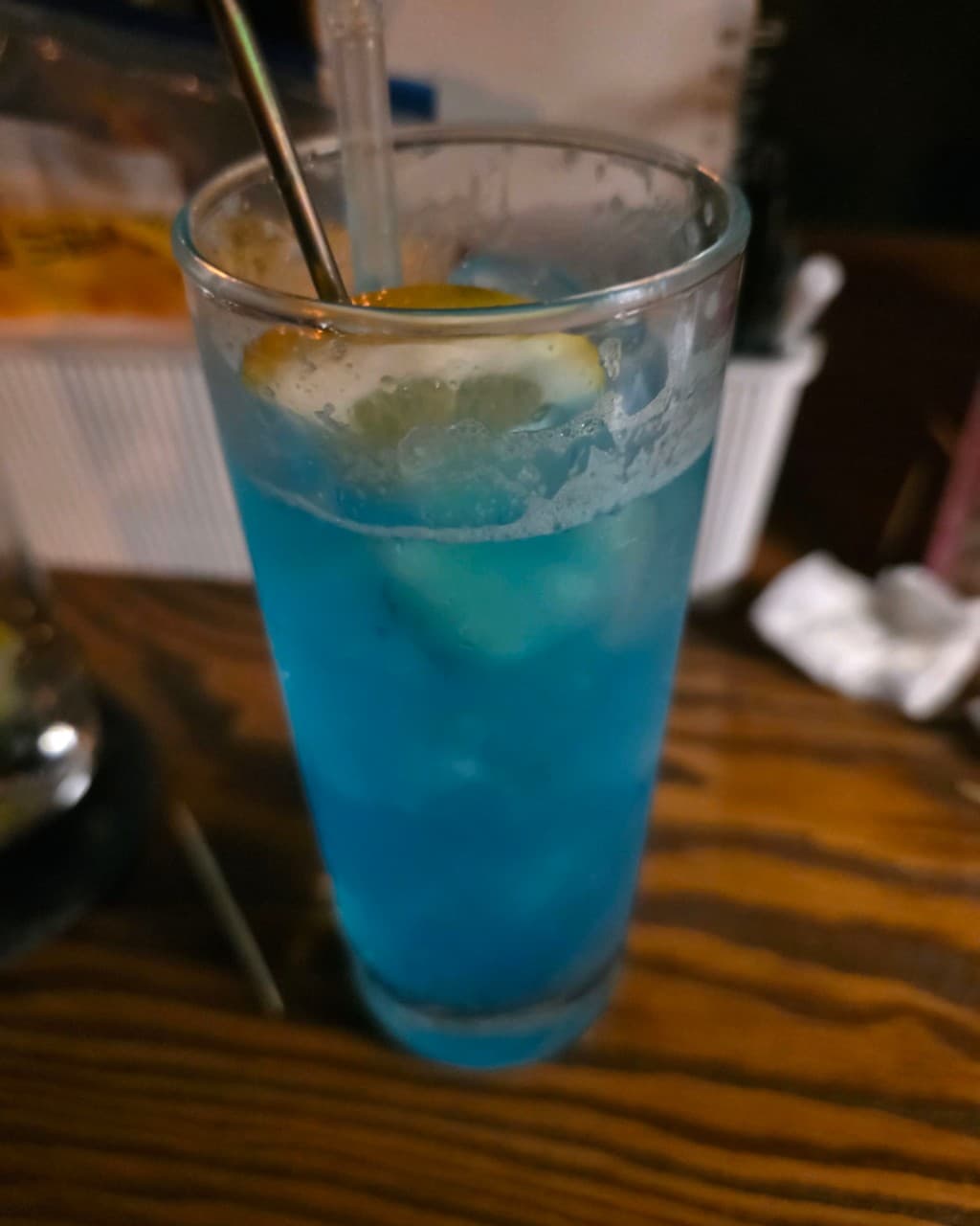 충청북도 청주시 제주아홉 혼술바 청주 지웰시티점 바(Bar) - 어두운 조명 아래 나무 다찌석에 놓인 레몬 띄운 파란색 하이볼과 1인 혼술 상황