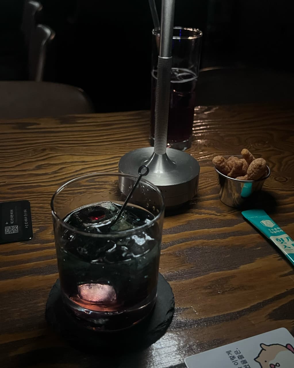 충청북도 청주시 야화 혼술바 청주율량점 바(Bar)의 어두운 조명 아래 나무 테이블 위 얼음 담긴 하이볼과 1인용 안주가 차려진 다찌석 혼술 공간