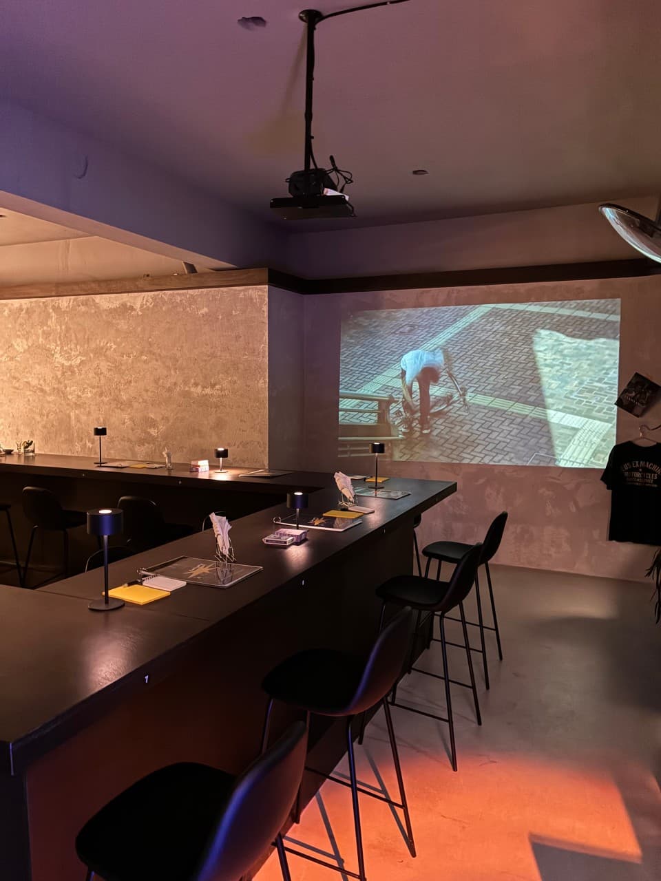 충청북도 청주시 잔향 혼술바 바(Bar) 내부. 빔프로젝터 영상이 상영되는 벽면과 개별 스탠드가 놓인 다찌석 1인 좌석. 낮은 조도의 조명 아래 놓인 검은색 테이블과 바 체어.