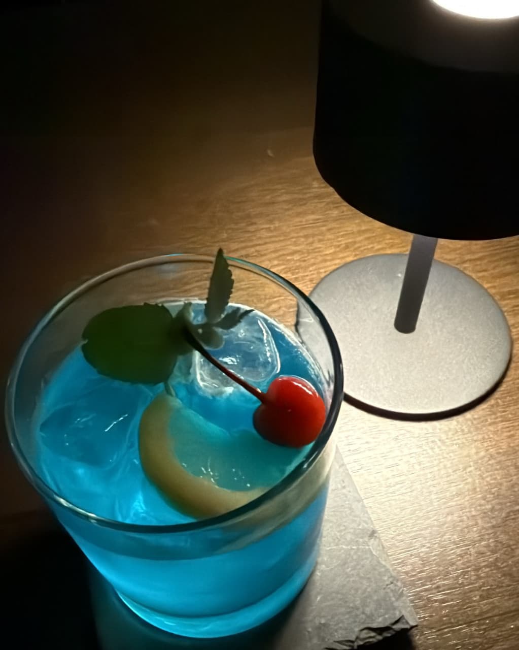 충청북도 청주시 잔향 혼술바 바(Bar)의 어두운 다찌석 위 핀 조명이 비추는 푸른 칵테일. 레몬과 체리가 담긴 1인 술잔이 놓여 혼술 중인 모습.
