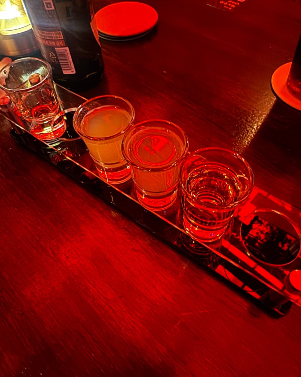 충청북도 청주시 온도홀술바 청주동남지구점 바(Bar) 1인 다찌석의 붉은 조명 아래 놓인 샘플러 술잔 네 개. 목재 테이블 위 투명한 액체가 담긴 잔이 혼술 상황을 보여줌.