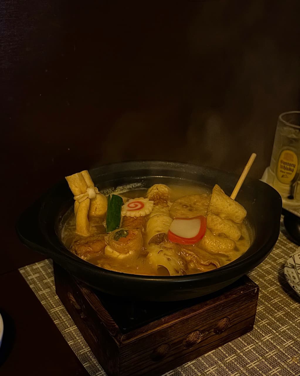 서울특별시 동작구 오뎅바 오락 다찌석에서 즐기는 혼술. 김이 나는 뚝배기 속 유부주머니와 어묵, 배후의 하이볼 한 잔이 조명 아래 배치된 1인 테이블 상황.