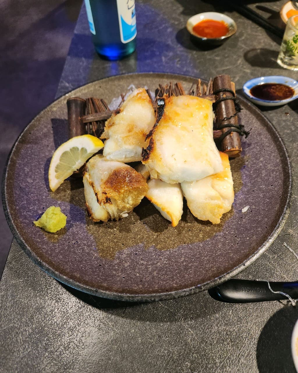 서울특별시 동작구 이자카야민 다찌석 1인 혼술 차림. 노릇하게 구운 생선살과 레몬, 와사비가 담긴 접시 옆으로 푸른 소주병이 놓인 이자카야 상황.