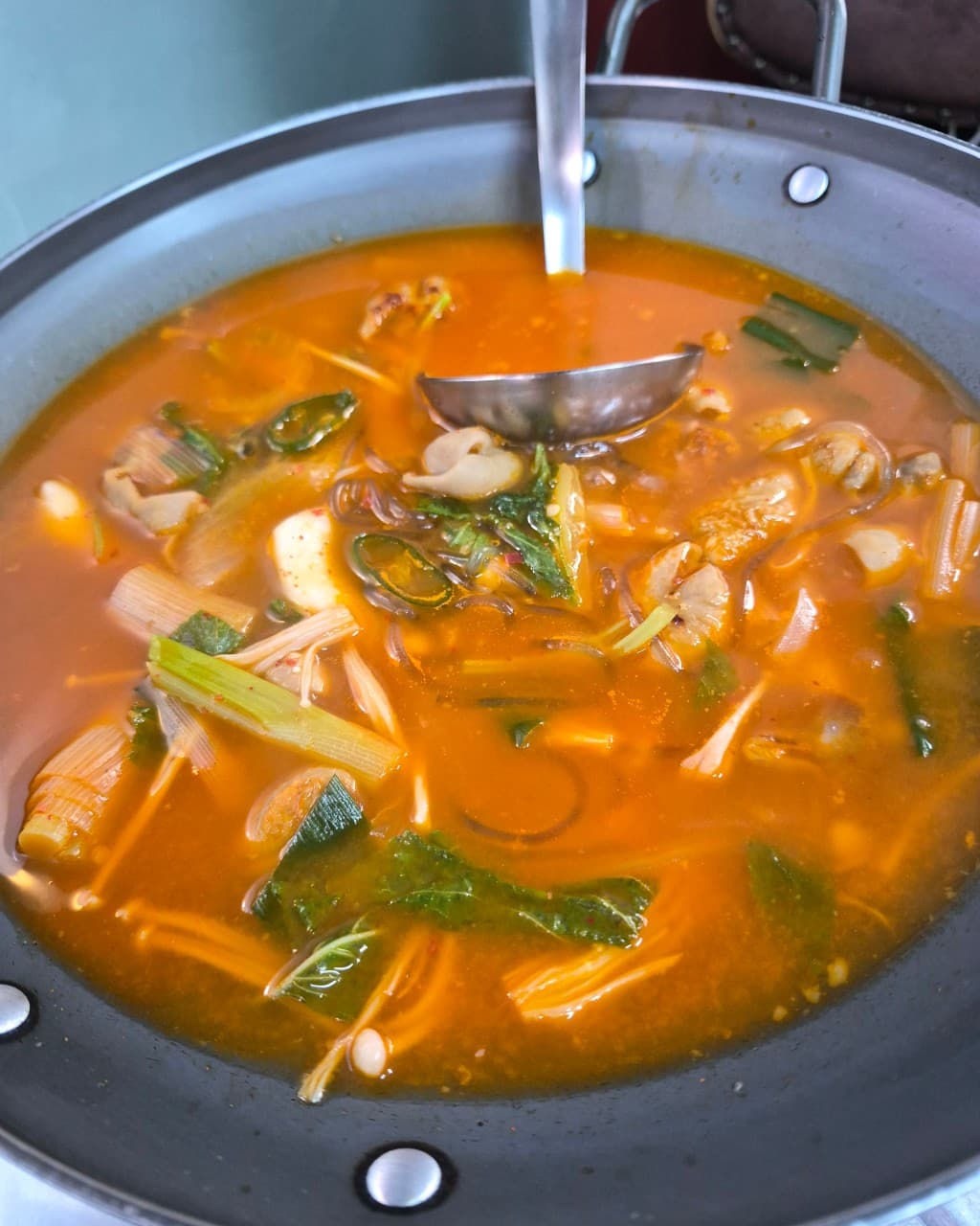 서울특별시 동작구 맥주 호프 그냥갈수없잖아 - 금속 전골 냄비 속 팽이버섯과 채소가 담긴 빨간 국물 요리. 1인 다찌석 조명 아래 차려진 혼술 식사 상황.