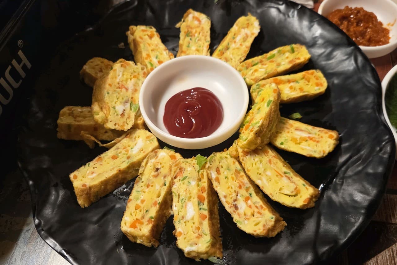 서울특별시 동작구 맥주 호프 그냥갈수없잖아 1인 혼술 안주인 야채 계란말이. 어두운 조명 아래 검은 접시에 원형으로 배치된 달걀말이와 중앙의 케첩.