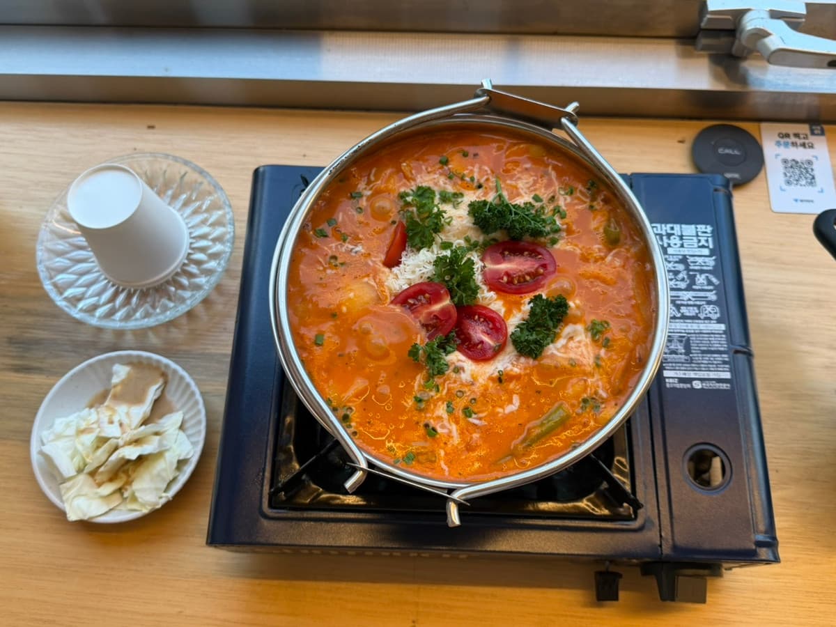 충청북도 청주시 미장센 이자카야 다찌석에서 즐기는 1인 혼술 - 가스버너 위 토마토 스튜와 치즈, 파슬리 고명이 올라간 냄비 요리와 양배추 샐러드 차림