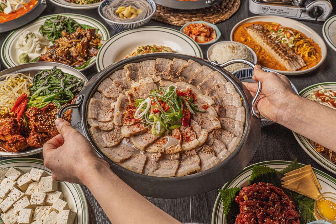 충청북도 청주시 요리주점 김씨형제 다찌석의 1인 수육 보쌈과 여러 안주. 노란 조명 아래 육즙이 보이는 고기 질감과 테이블 가득 차려진 음식으로 혼술을 즐기는 상황.